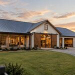 Modern barndominium with wraparound porch and garage at sunset